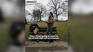 An Old Man Sits On A Public Bench With A Millennial W