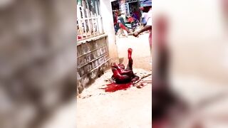 A Man Lies In The Street Being Attacked By A Man With A Machete