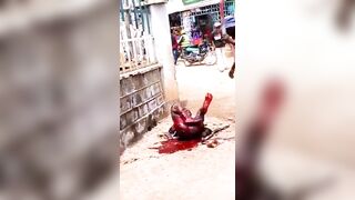 A Man Lies In The Street Being Attacked By A Man With A Machete